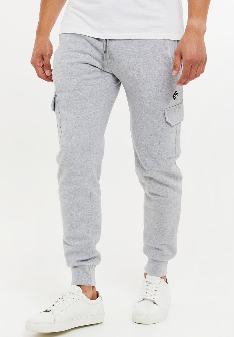 Grå mjukisbyxor med avsmalnande passform, sidofickor med lock och elastiska muddar; matchade med vita sneakers. Tillverkade av mjukt bomullsblandat material.