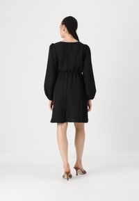 Melna īsā kleita ar puffētiem garajiem piedurkņu, sašaurinātu jostasvietu un gludu tekstūru. Tam ir apaļa dekoltē forma un tas krīt tieši virs ceļgaliem.