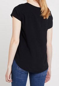 T-shirt nero a maniche corte con orlo curvo, texture liscia e dettagli di cucitura minimi, indossato con jeans in denim blu.