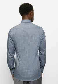 Langärmeliges Hemd in Blau mit geometrischem Muster. Hergestellt aus glattem Stoff, mit spitzem Kragen und einreihigen Knopfmanschetten.