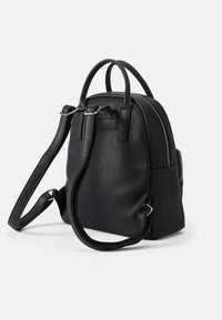 Mochila de couro preto com forma arredondada, duplas alças superiores, alças ajustáveis e fecho com zipper. Superfície texturizada com hardware minimalista.