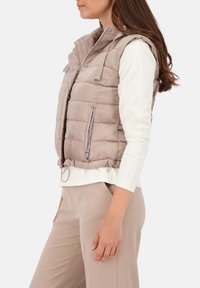 Gepolsterte ärmellose Weste in hellem Beige mit leicht glänzender Oberfläche, ausgestattet mit einem Reißverschluss vorne, seitlichen Taschen und einem hohen Kragen.