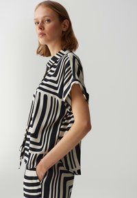 Schwarz-weiße gemusterte Bluse mit kurzen Ärmeln, rundem Kragen und Knöpfen an der Vorderseite. Hergestellt aus einem leichten, strukturierten Stoff.