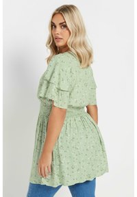 Green floral blouse with short ruffled sleeves, smocked waist, and a flowing design. Soft fabric with a light texture and delicate patterns.