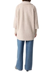 Beige strukturierte Jacke mit breitem Kragen, oversize Passform und Dreiviertelärmeln, kombiniert mit hellblauen weit geschnittenen Jeans.