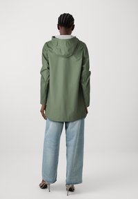 Grön vattentät jacka med huva, långa ärmar och lös passform, kombinerad med ljusblå vida jeans. Slät yta, minimalistisk design.