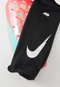 Juodas tinklinis kojinės su balta Nike logotipu, derinamas su raudonu ir turkio spalvos apsauginiu įrankiu su tekstūruotomis skylėmis ir Superlock prekės ženklu.