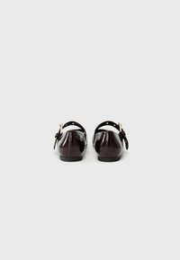Ballerines en cuir bordeaux foncé avec un bout arrondi, une fine sangle avec des accessoires dorés à l'arrière, et une semelle noire plate.