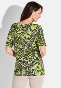 Korte mouw top in groen met abstracte zwarte, grijze en gele spiraalpatronen. Heeft een ronde halslijn en een getailleerde pasvorm.