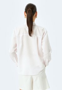 Camisa de manga larga a rayas rosa claro con puños abotonados y yugo en la parte posterior, confeccionada en un tejido suave, combinada con pantalones cortos blancos.