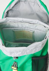 Žalias kuprinė su pilku interjeru ir raišteliu uždarymui. Turi tinklines šonines kišenes ir spausdintą etiketę daiktams organizuoti.