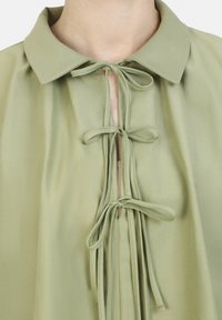 Blusa verde claro con cuello, que presenta un escote en forma de lágrima y detalles atados. Confeccionada en una tela suave con una textura suave y fluida.