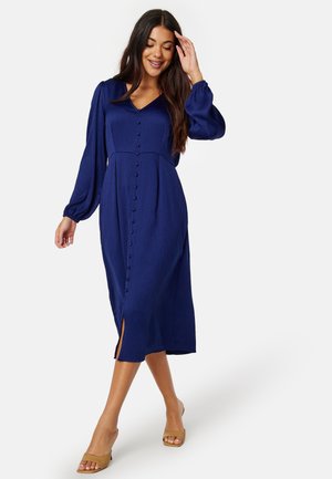 Robe midi bleu marine avec de longues manches bouffantes, décolleté en V et une rangée de boutons sur le devant. Le tissu a une finition texturée et une fente sur le côté.