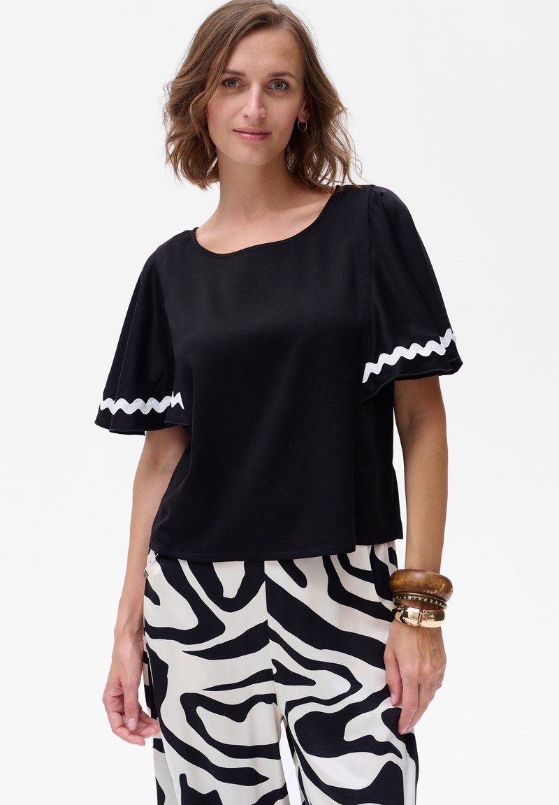 Zwart T-shirt met korte mouwen en een gegolfde witte rand bij de mouwen, gecombineerd met beige broek met een zwart zebra-strepenpatroon.