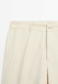 Beige linnebyxor med flat front, sidofickor och knappstängning. Har en slät textur och rena linjer i designen.