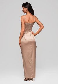 Widok z tyłu długiej, eleganckiej beżowej sukni satynowej z cienkimi ramiączkami i dopasowanym gorsetem, zdobionej subtelnym wzorem w kropki oraz prostą sylwetką.