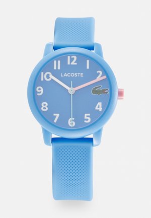 Modra silikonska ura s okroglo obliko, belimi označevalci ur in roza sekundo. Ima majhen logotip krokodila na obrazu in teksturiran trak.