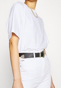 Camiseta blanca de algodón con mangas cortas, combinada con unos vaqueros blancos de cintura alta y un cinturón de cuero negro con una hebilla de plata detallada.