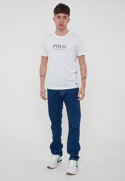 T-shirt bianca in cotone con logo "POLO RALPH LAUREN", abbinata a jeans in denim blu e sneakers bianche con accenti verdi.