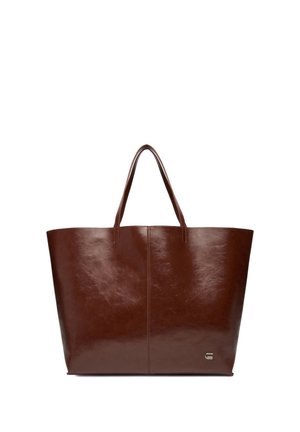 Bolso tote de cuero marrón con asas dobles y un pequeño emblema de logo metálico en la esquina inferior derecha, mostrado sobre un fondo blanco.