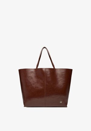 Braune Ledertasche mit zwei Griffen und einem kleinen Metall-Logosymbol in der unteren rechten Ecke, vor weißem Hintergrund gezeigt.