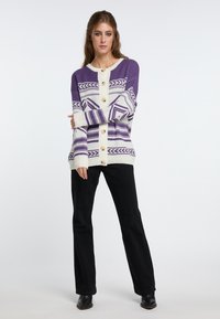 Lila och krämfärgad stickad cardigan med geometriska mönster, lätt textur och träknappar, parat med svarta utsvängda byxor.