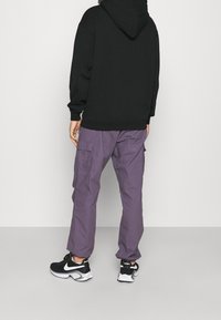 Černá mikina s kapucí, volný střih, spárovaná se světle fialovými cargo kalhotami s bočními kapsami. Na nohou černé a bílé sportovní tenisky.
