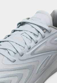 Κοντινό πλάνο ανοιχτόχρωμου γκρι αθλητικού παπουτσιού Reebok με υφασμάτινη υφή, λεπτομερή ραφές και σφιχτά δέσιμα επίπεδα κορδόνια.