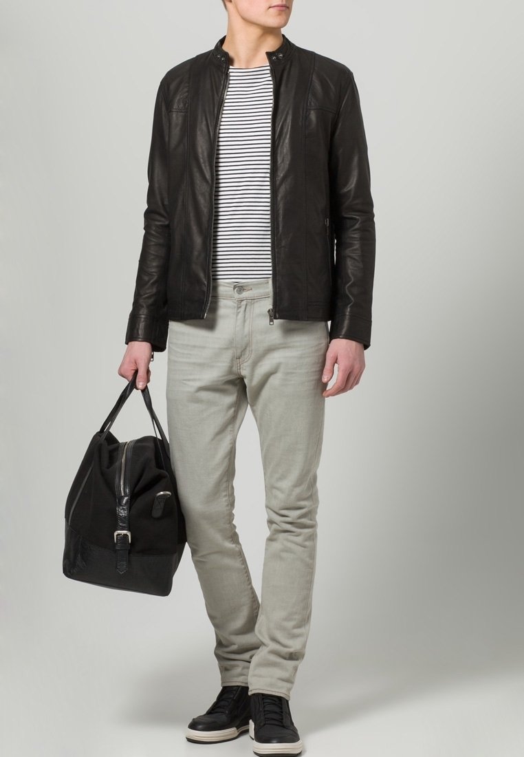 Homme portant une veste en cuir noire, une chemise rayée, un pantalon gris clair et des baskets noires, tenant un sac de sport noir.
