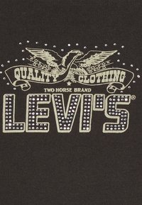 Černé tričko s texturovanou grafikou, kterou zdobí stříbrné hroty, design orla a nápis "LEVI'S" v tučném písmu.