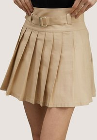 Gonna beige plissettata con una vita alta e dettaglio con fibbia. Il tessuto è liscio con un design strutturato, caratterizzato da pieghe profonde e uniformi.