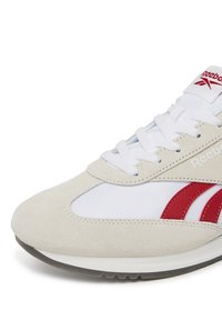 Białe sneakersy z beżowym zamszowym noskiem, czerwonymi skórzanymi akcentami po bokach i białymi sznurówkami. Posiadają amortyzowaną podeszwę dla komfortu.