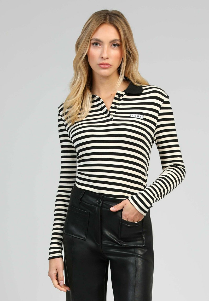 Polo à manches longues rayé noir et blanc avec un col, comportant une étiquette à l'avant avec l'année "1985" et accentué avec un pantalon en cuir noir ajusté.