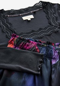 Czarny top z prążkowanej tkaniny z koronkowym wykończeniem; kolorowe spodnie na elastycznej talii z wielokolorowym wzorem kwiatowym w odcieniach niebieskiego, fioletowego i różowego.