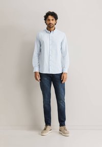Hellblau gestreiftes Hemd mit Knopfverschluss, langen Ärmeln und klassischem Kragen, kombiniert mit dunklen Jeans und beigen Turnschuhen.