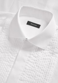 Valge särk, millel on struktureeritud esipind vertikaalsete pintuck detailidega, tavaline krae ja must silt, millel on sees "Martinique".