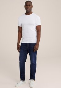 Witte t-shirt met korte mouwen, aansluitend ontwerp. Donkerblauwe jeans met een rechte pasvorm. Witte sneakers, gladde textuur en klassieke stijl.