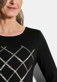 Schwarzes Langarmoberteil mit einem silbernen Pailletten-Diamantmuster auf der Vorderseite, rundem Ausschnitt und weichem Stoffgefühl.