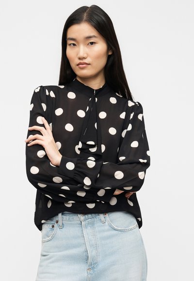 Μαύρη μπλούζα με μεγάλα λευκά πουά, φουσκωτά μανίκια με πτυχωτό σχεδιασμό και δέσιμο στον λαιμό. Συνδυάζεται με ανοιχτόχρωμα μπλε τζιν. Διαφανές, αέρινο ύφασμα.