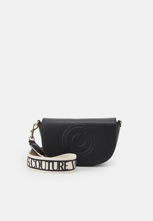 Zwarte leren crossbodytas met klepsluiting, geperst rond logo aan de voorkant en afneembare witte band met zwarte Versace Jeans Couture lettering.