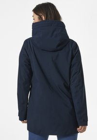 Chaqueta impermeable de color azul marino con capucha, presenta un diseño aerodinámico, textura suave y puños ajustables. Vista trasera.