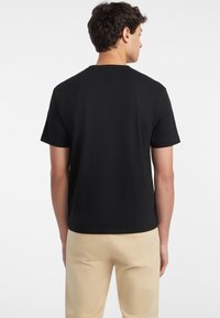 Schwarzes kurzärmliges T-Shirt mit Rundhalsausschnitt, aus weichem Stoff, mit schlichter Gestaltung und lockerer Passform. Kombiniert mit hellen Khakihosen.