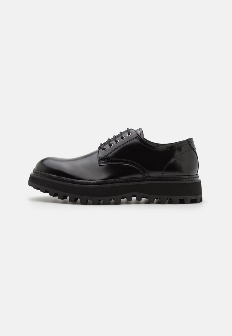 Chaussure noire en cuir verni à lacets, avec une semelle épaisse et crantée, vue de profil sur un fond blanc uni.