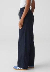 Pantalon large bleu marine avec une taille élastique et un cordon de serrage. Doté de coutures contrastées et de poches latérales pour plus de praticité.