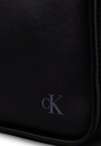 Czarna skórzana torba o teksturowanej powierzchni, z subtelnym wytłoczonym logo "cK". Zorganizowany design z gładkimi akcentami.