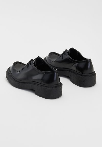 Zapatos de cuero negro con un acabado brillante, puntera redonda y suela de goma gruesa y texturizada. Presenta cordones y detalles de costura mínimos.