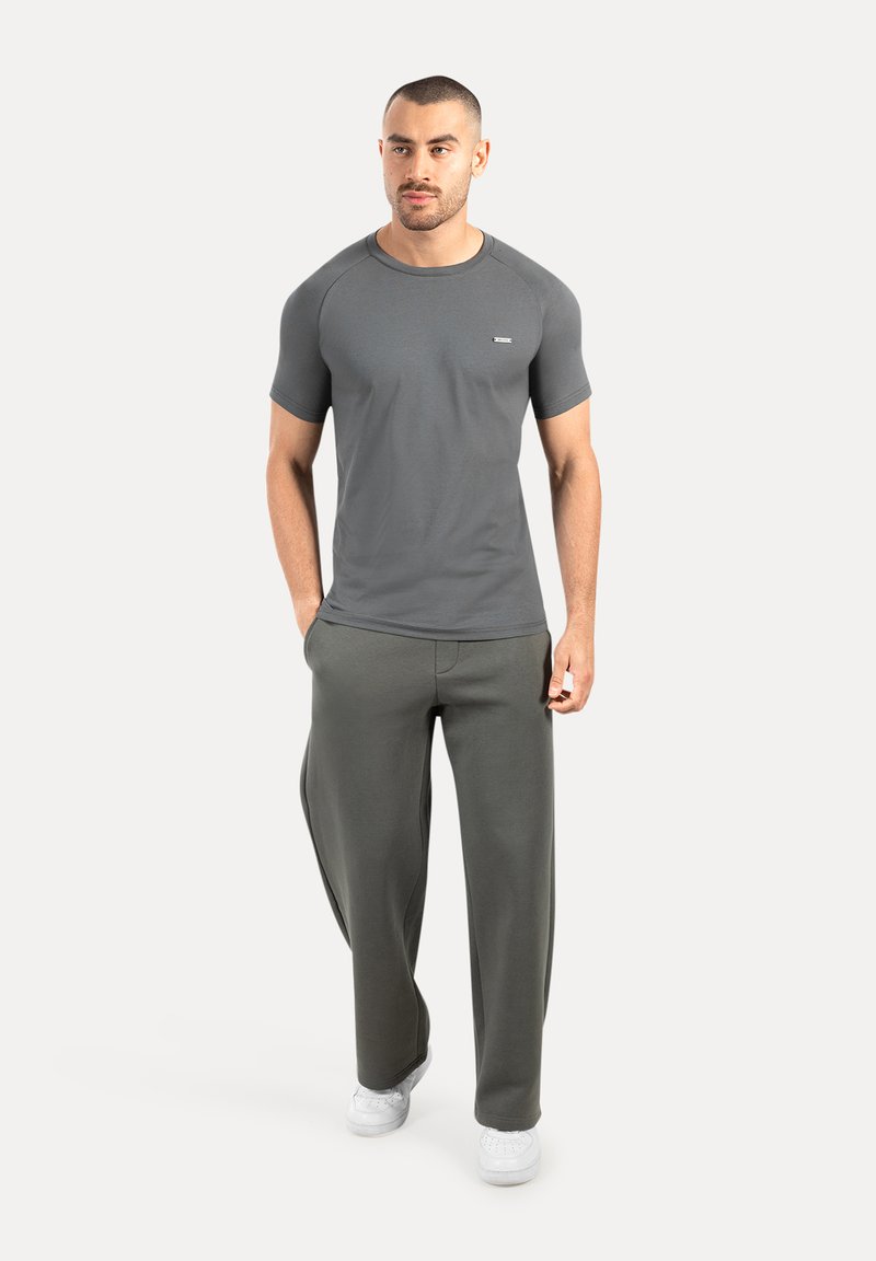 Camiseta deportiva gris de manga corta y cuello redondo, combinada con pantalones verdes sueltos y zapatillas blancas. Diseño sencillo y funcional.