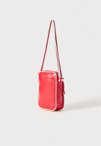 Borsa a tracolla sintetica rossa con piping bianco, dotata di una tasca con zip e di una tracolla regolabile a righe. Design compatto e rettangolare.