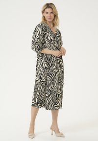 Black and cream zebra print dress with a deep V-neck, three-quarter sleeves, and a relaxed fit, paired with cream heeled mules.