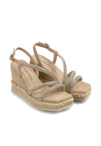 Beige wedge sandals with a textured suede finish, featuring metallic straps and a braided rope accent around the sole. Square toe design.